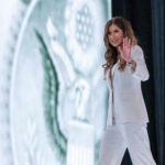 Person in white suit waves on stage background