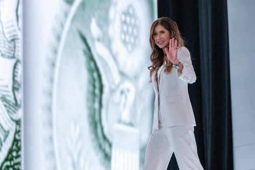 Person in white suit waves on stage background