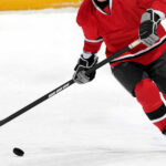 Hockey player in red jersey skating with puck.