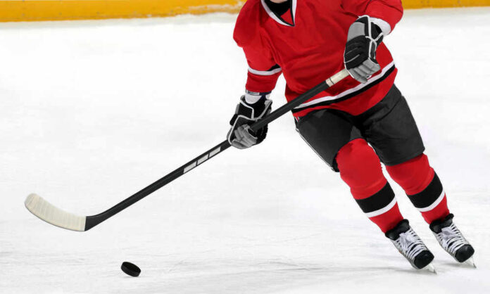 Hockey player in red jersey skating with puck.