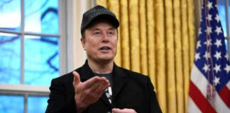 Man wearing hat gesturing in room with flag