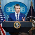 Man speaking at podium with flags in background