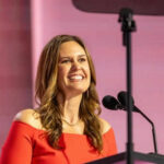 Woman in red dress speaking at podium smiling