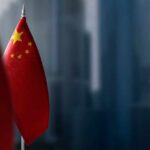 Is China’s Fighter Fleet Outgrowing America’s? Close-up of the Chinese flag on a flagpole with a blurred urban background