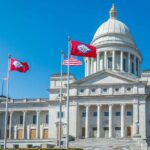 State capitol building with flags in front against a clear blue sky