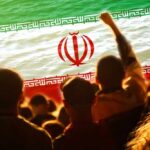 Crowd of people with their hands raised in front of the Iranian flag