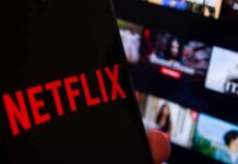 Close-up of a smartphone displaying the Netflix logo with a blurred background of movie thumbnails