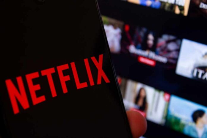 Close-up of a smartphone displaying the Netflix logo with a blurred background of movie thumbnails