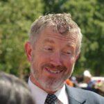 A smiling man in a suit engaging in conversation outdoors