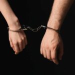 Parents Charged: Infant’s Tragic Abuse Unveiled Two hands connected by handcuffs against a dark background