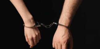 Two hands connected by handcuffs against a dark background