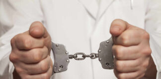 A person in a white coat holding handcuffs tightly