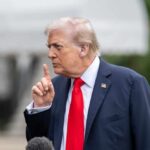 A man in a suit gesturing with his finger during a press conference