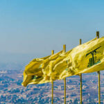 Multiple yellow flags waving in the wind against a clear sky