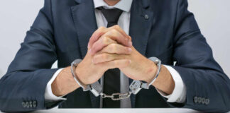 A man in a suit with hands handcuffed together on a table