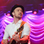Musician performing on stage with a guitar under colorful lights