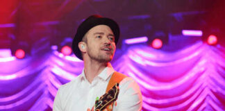Musician performing on stage with a guitar under colorful lights