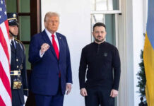 Two men standing outdoors near flags and doorway