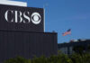 CBS sign on building, American flag in background.