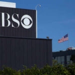 CBS sign on building, American flag in background.