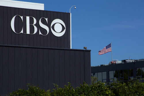 CBS sign on building, American flag in background.