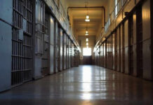 Empty prison corridor with barred cell doors visible