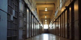 Empty prison corridor with barred cell doors visible