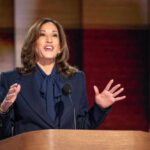 Person speaking at podium with American flags behind