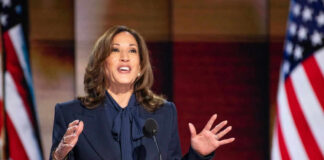 Person speaking at podium with American flags behind
