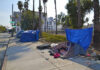 Tents and tarps line sidewalk near palm trees