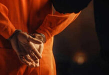 Person in orange jumpsuit with hands cuffed behind back