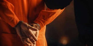 Person in orange jumpsuit with hands cuffed behind back