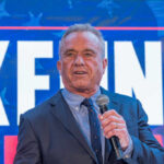 Man speaking in front of large sign with microphone