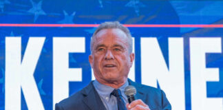 Man speaking in front of large sign with microphone