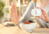 Person holding an alarm clock with a bowl of cereal in front