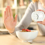 Person holding an alarm clock with a bowl of cereal in front
