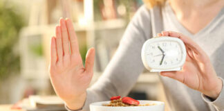 Person holding an alarm clock with a bowl of cereal in front
