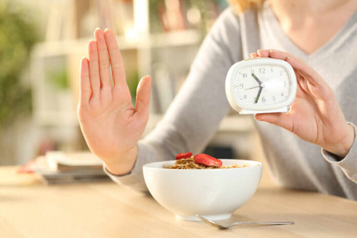 Person holding an alarm clock with a bowl of cereal in front