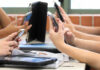 Students' hands holding smartphones in a classroom