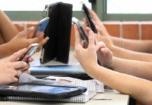 Students' hands holding smartphones in a classroom