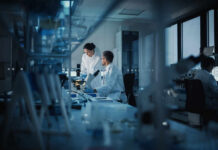 Two scientists working in a laboratory with a microscope and computer screens