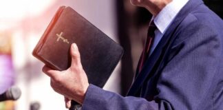 A person in formal attire holding a Bible while speaking