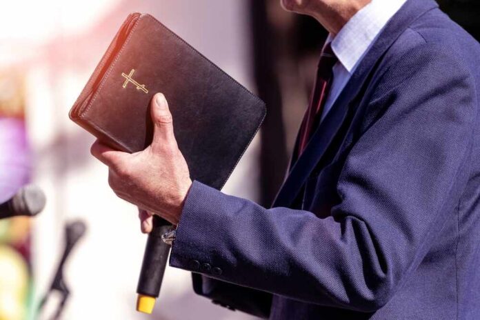 A person in formal attire holding a Bible while speaking