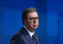 A political figure in formal attire with a serious expression during a press conference