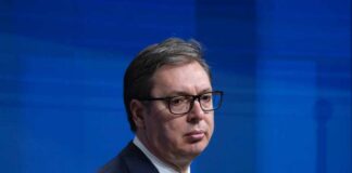 A political figure in formal attire with a serious expression during a press conference