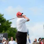 A golfer in a red cap swings a golf club at an outdoor event