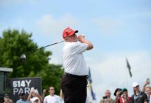 A golfer in a red cap swings a golf club at an outdoor event