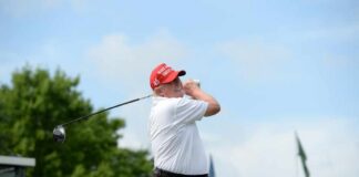 A golfer in a red cap swings a golf club at an outdoor event
