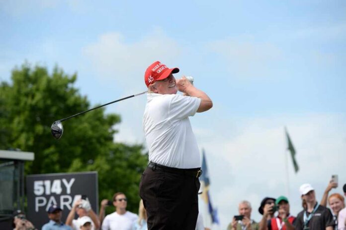 A golfer in a red cap swings a golf club at an outdoor event