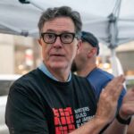 Person clapping at a protest wearing a Writers Guild of America t-shirt